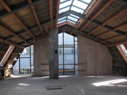 Dachgeschoss mit Holzrahmen, großen Fenstern und unvollendeter Innenwand.