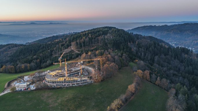 Landschaft mit Hügeln, Bäumen und einer Baustelle im Vordergrund bei Sonnenaufgang.