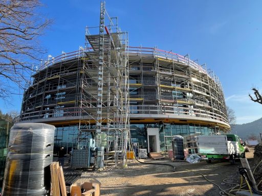Neubau mit Gerüst und Bauarbeiten, umgeben von Baustellenmaterial.